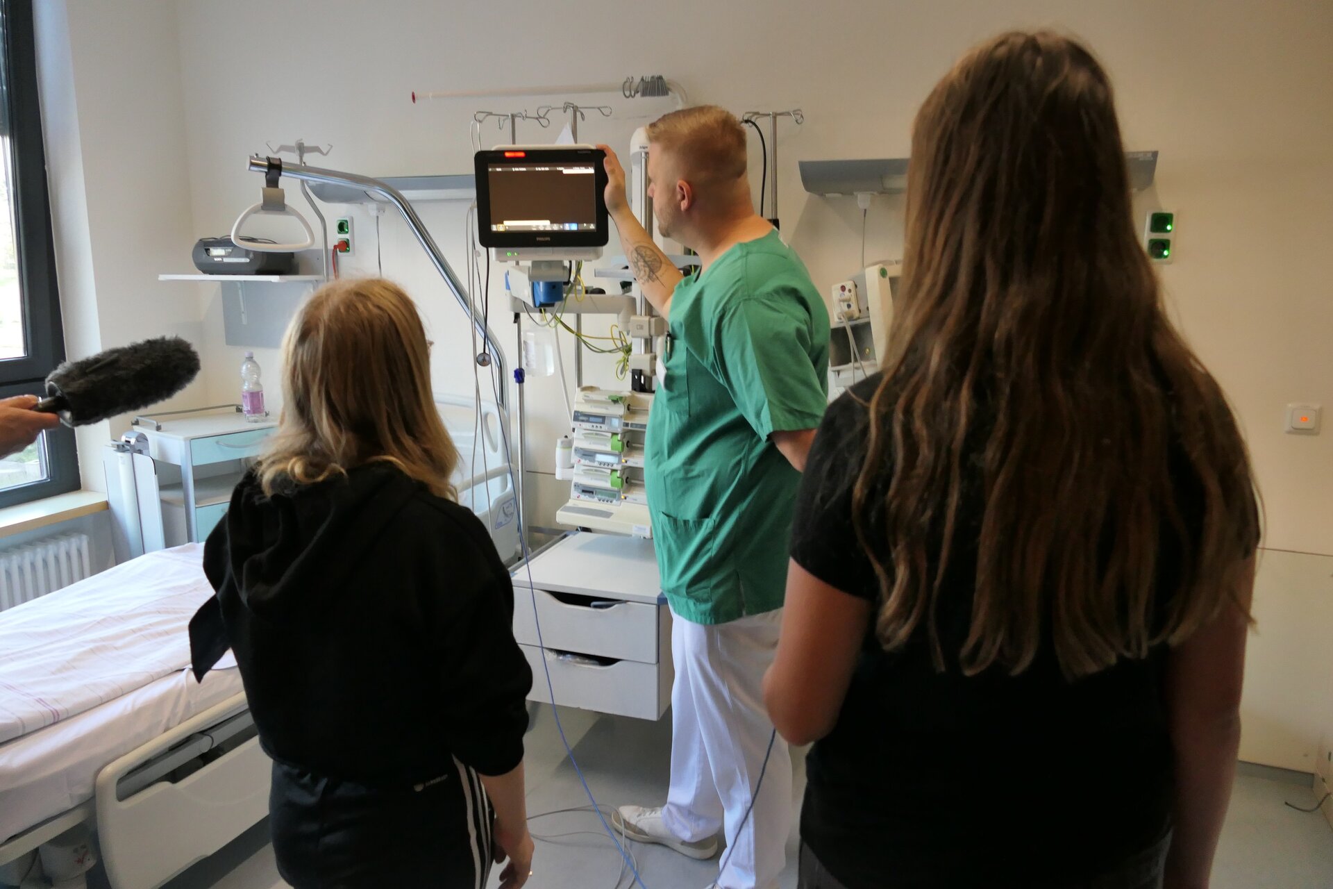 Azubi-Dating 2023 Zwei Jugendliche stehen mit einer Pflegekraft in einem Krankenhauszimmer