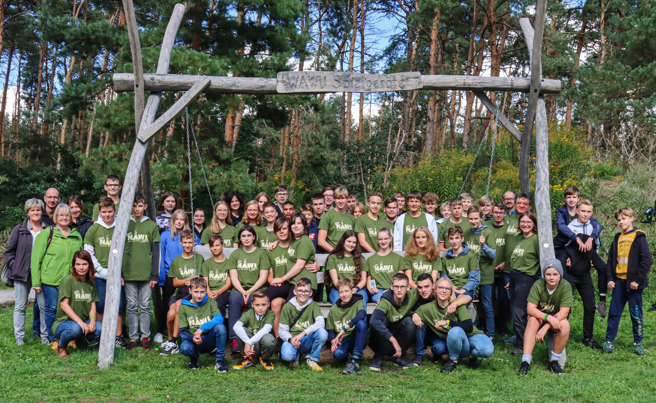 Gruppenfoto mit vielen Jugendlichen, die vor einer großen Holzschaukel stehen