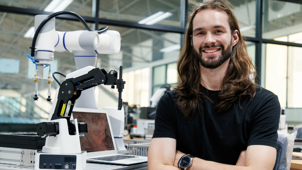 Junger Mann mit langen braunen Haaren, der neben einem Roboter steht