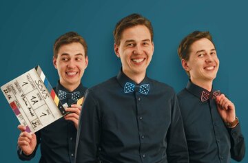 Florian Arndt Junger, lachender Mann mit dunklem Hemd und blauer Fliege, einmal im Vordergrund, zweimal im Hintergrund. Mann im Hintergrund links hält Filmklappe